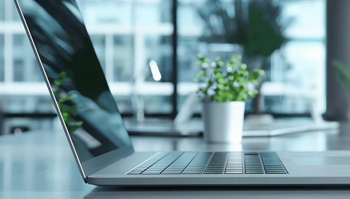 Ein offenes Laptop mit modernem Design, neben einem Topf mit Pflanzen, in einem hellen, inspirierenden Raum.