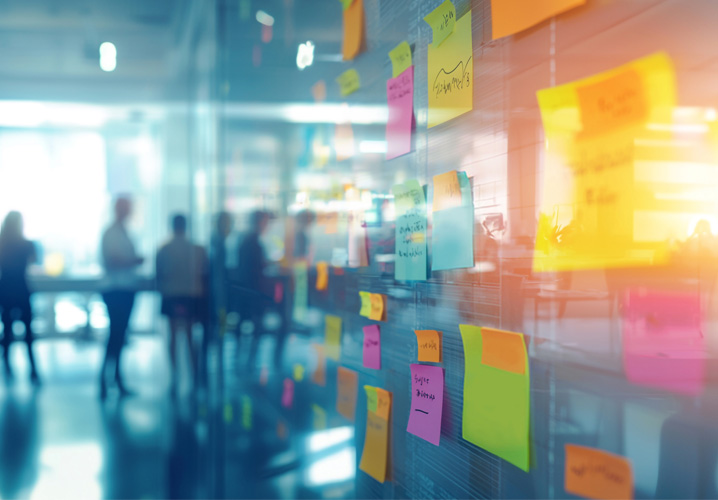 Bunte Haftnotizen an einer Glaswand, unterstützt durch Benefit Beratung, die kreatives Brainstorming und Teamarbeit in einem modernen Büro darstellen.