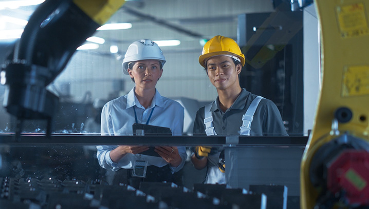 Fachkräfte im Werk, durch betriebliche Arbeitskraftabsicherung geschützt, betrachten Maschine.