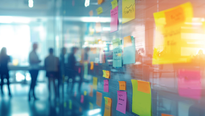 Bunte Haftnotizen an einer Glaswand, unterstützt durch Benefit Beratung, die kreatives Brainstorming und Teamarbeit in einem modernen Büro darstellen.