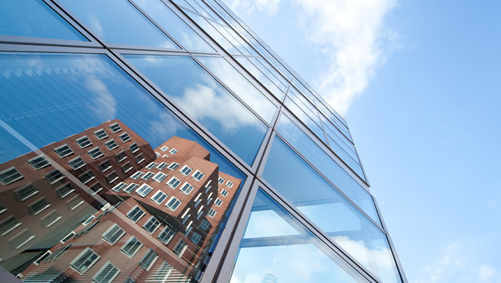 Eine gläsernde Fassade, in der sich ein weiteres Gebäude spiegelt. 