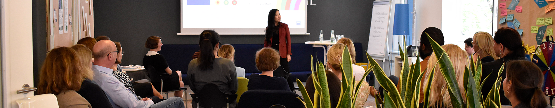 Eine Präsentation von Wanlu Wei in einem modernen Raum, mit Zuhörern, die aufmerksam der Rednerin folgen. 