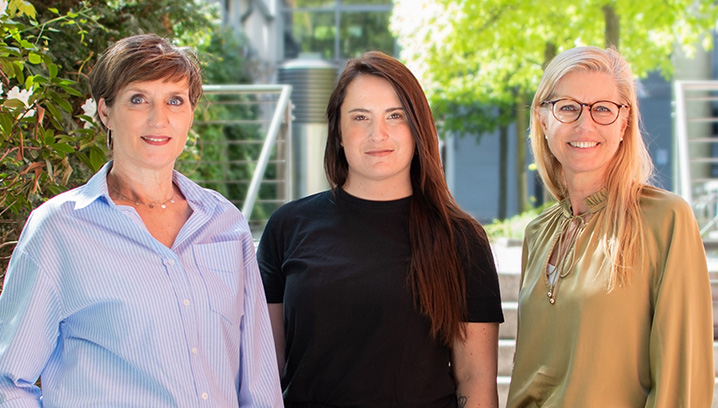 Gruppenfoto von Anke Ungnade, Gianna-Isabell Ongaro und Dorothee Becker vor einem neutralen Hintergrund mit warmen Farben und Pflanzen.