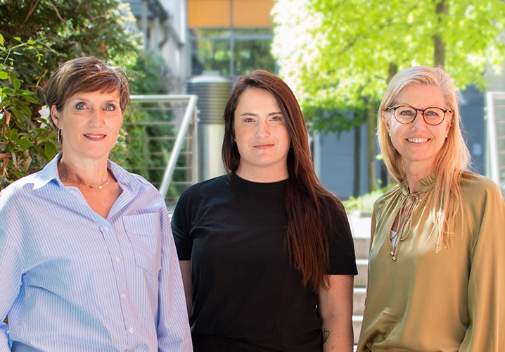 Gruppenfoto von Anke Ungnade, Gianna-Isabell Ongaro und Dorothee Becker vor einem neutralen Hintergrund mit warmen Farben und Pflanzen.
