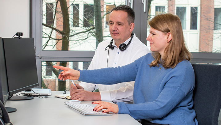 Zwei Personen im Büro konzentriert am Computer, die Frau zeigt etwas auf dem Bildschirm. Kooperative Atmosphäre.