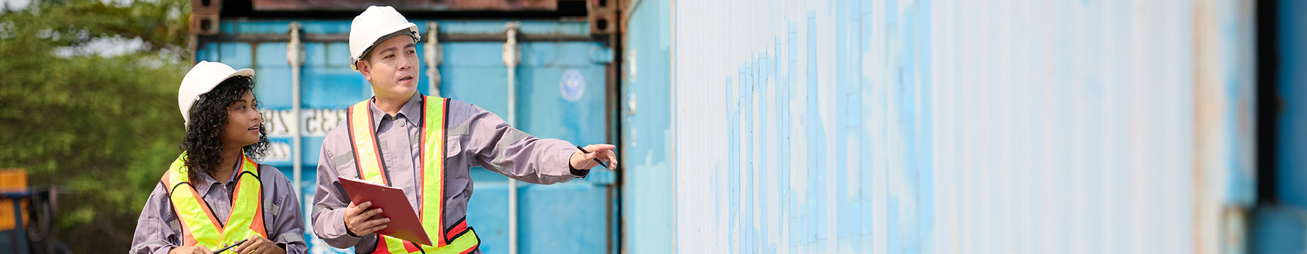 Zwei Menschen in Schutzkleidung besprechen den Zustand der Container, der Fokus liegt auf Teamarbeit.