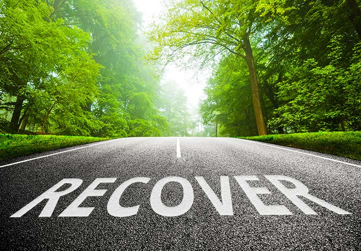 Eine Straße mit dem Schriftzug "Recover", die in einen grünen Wald führt