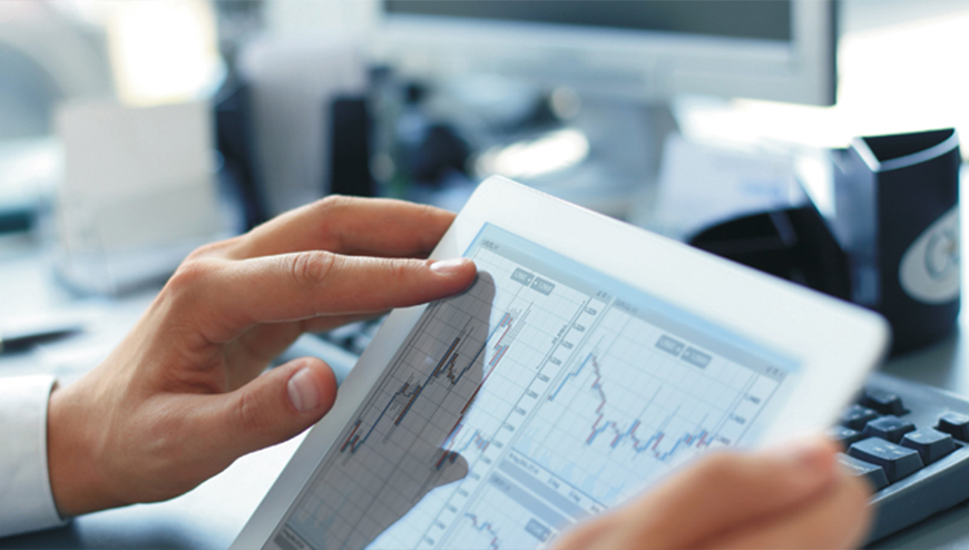 Eine Hand hält ein Tablet mit Finanzdiagrammen, vermittelt Konzentration und moderne Technologie am Arbeitsplatz.