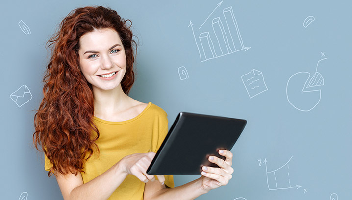 Lächelnde junge Frau mit einem Tablet vor einer grafischen Wand, die Optimismus und Produktivität ausstrahlt.