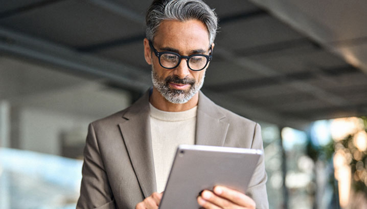 Mann mit grauen Haaren und Brille, der konzentriert ein Tablet in einem modernen Umfeld betrachtet.