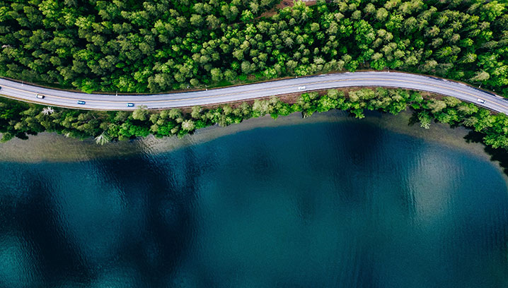 Kurvenreiche Straße am Ufer eines tiefblauen Sees, umgeben von sattem Grün. Ruhige, idyllische Stimmung.