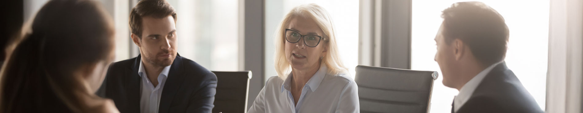 Frau spricht im Meeting, strahlt Autorität aus, Männer hören aufmerksam zu. Spannung und Konzentration im Raum.