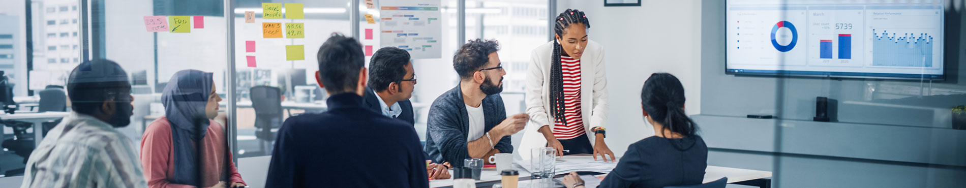 Diverse Gruppe diskutiert engagiert in einem modernen Meetingraum mit Datenvisualisierungen.