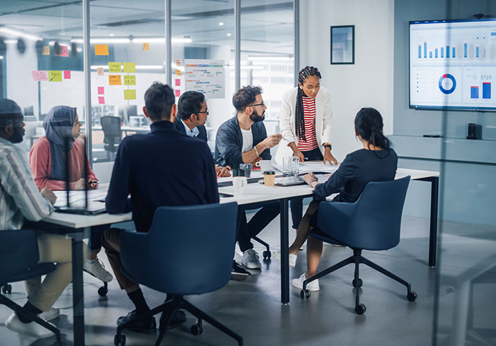 Diverse Gruppe diskutiert engagiert in einem modernen Meetingraum mit Datenvisualisierungen.